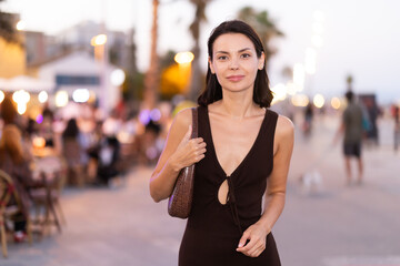 Fototapeta premium Smiling girl walks around old city district Barceloneta, pedestrian promenade embankment. People are walking by. Person in city, city bustle.