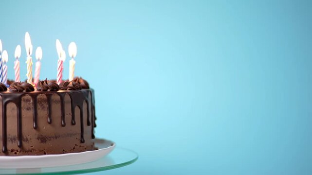 Lit candles adorn a decadent chocolate cake on a plain background.