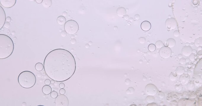 Soft abstract beauty background with delicate oil bubbles floating in clear liquid, illuminated by gentle light to create a clean cosmetic texture. Slow motion.