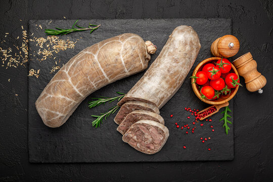 Top view of sliced meat headcheese on black slate background. Flat lay of meat terrine with rosemary, tomatoes and scattered spices