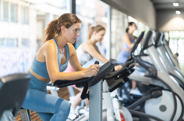 Fototapeta premium Woman in sportswear doing a workout on an exercise bike in the gym. European woman bought a fitness subscription for an athletic body