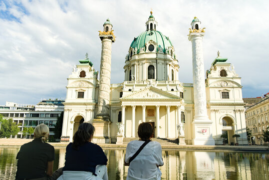 Three women sitting by the reflection pond at Karlskirche (St. Charles Church) in Vienna, Austria at sunset.