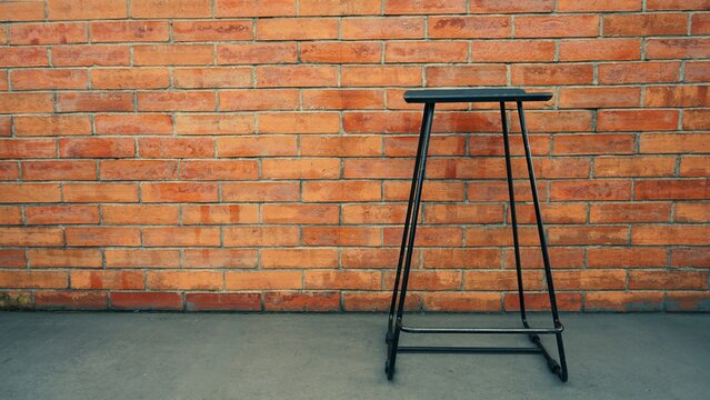 Single black metal bar stool against a red brick wall.