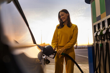 Woman driver standing at gas station holding fuel nozzle and filling her car with gas or petrol...