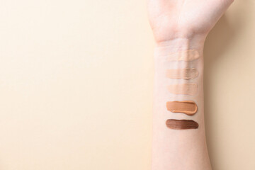 Woman with different shades of foundation on her arm against beige background, top view. Space for...