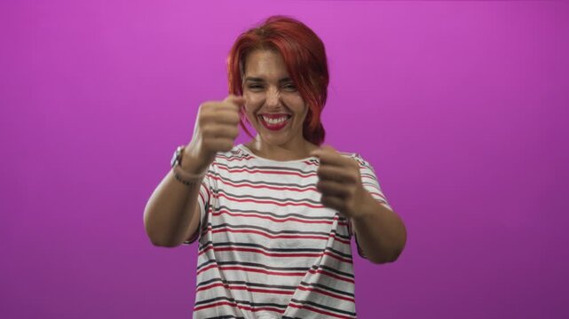 Woman smiling and gripping an imaginary steering wheel with both hands in magenta studio, wearing striped shirt and bracelets; joyful play.