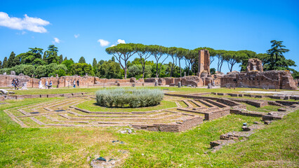 Naklejka premium Visitors explore the Domus Flavia ruins at the Roman Forum in Rome, Italy. This historical site features remnants of structures surrounded by greenery under a bright sky.
