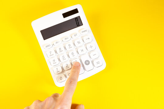 Calculator on a yellow background with finger pointing at the display