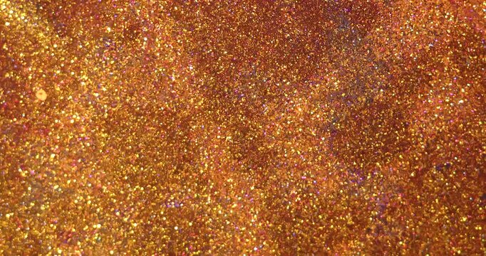 Abstract background with shiny gold and pink glitter on the surface of a liquid, creating dramatic fluid texture for creative design and modern art concepts. Slow motion.