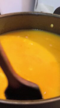 close view of boling pumkin and noodles soup in a metal pot on top of a stove
