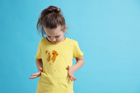 Little girl with stained shirt on light blue background. Space for text