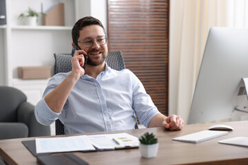 Naklejka premium Man talking on smartphone at wooden desk indoors