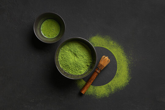 Bowl of fresh matcha tea with powder and chasen on black grunge background