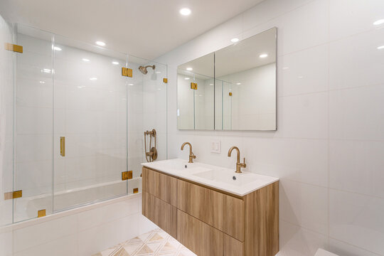 Modern white bathroom interior with double vanity, glass shower and brass fixtures