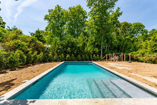 Newly built rectangular backyard swimming pool with entry steps in unfinished landscaped yard