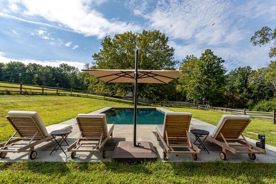 Backyard swimming pool with lounge chairs and umbrella in landscaped country setting
