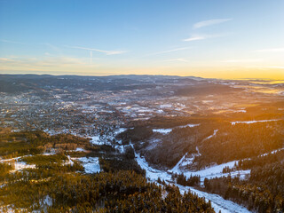Naklejka premium The scene shows a winter morning landscape in Liberec from a drone's view. Snow-covered hills and valleys stretch across the area with a warm light from the rising sun.