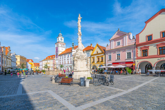TREBON, CZECHIA - JULY 14, 2024: People enjoy their time in Masaryk Square located in Trebon, Czechia. The sun shines bright as visitors gather around cafes and admire the buildings and fountain.