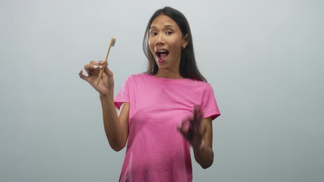Young woman holding a bamboo toothbrush in hand and inspecting it while making an ok gesture in studio; oral care confidence.
