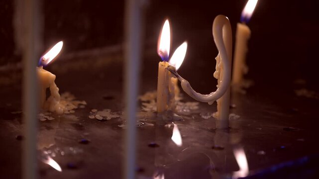 A candle burns softly, casting warm light through the gap of heavy metal doors