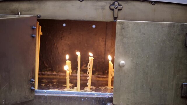 A candle burns softly, casting warm light through the gap of heavy metal doors