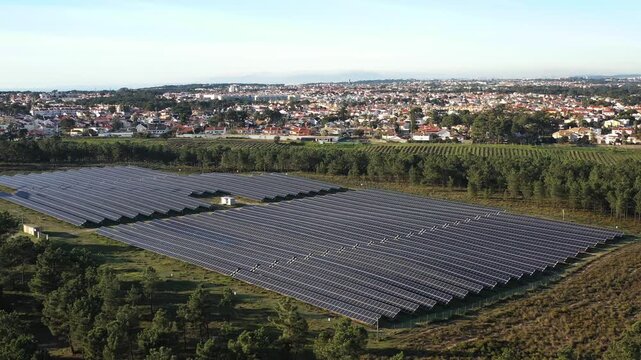 Aerial drone shot of solar panels installed on field in countryside under clear sky, emphasizing renewable energy and sustainability, with townscape in the distance