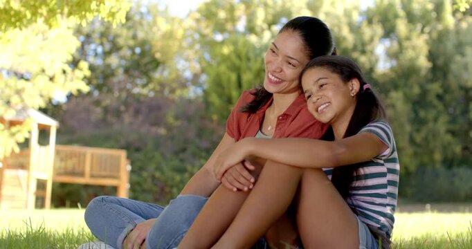 African American mom and teen daughter watching offscreen play, leaning in park near playset