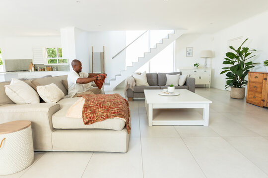 African American man sitting on chaise folding rust blanket in living room sectional, copy space