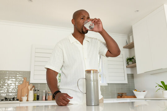 Man wearing light short-sleeve collared shirt raising glass at kitchen island near stainless carafe