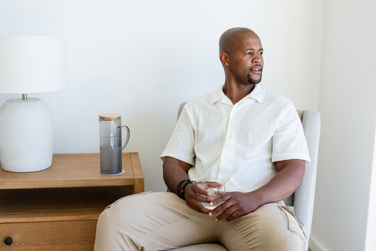 Man sitting in armchair hearing offscreen cue, holding glass and spawning animated hydration chart