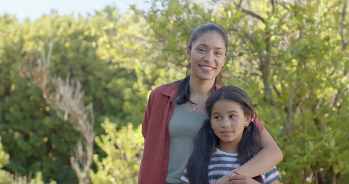 Leaning mother in green top and necklace hugging daughter in park, camera tightening, showing love