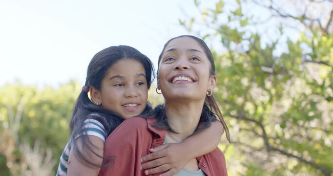 African American mother and daughter giving piggyback ride in park, child pointing at treetops