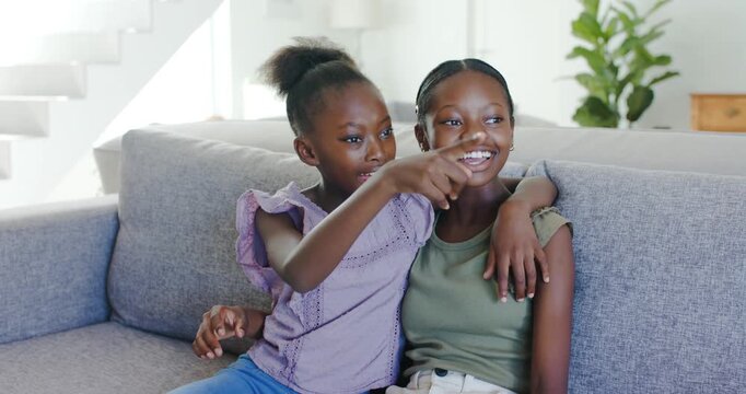 African American sisters sitting on grey sofa child talking draping arm pointing right teen smiling