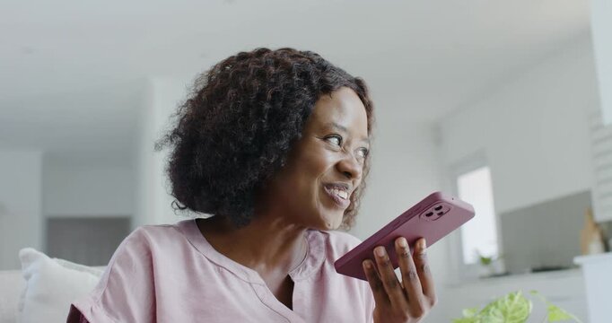 African American woman getting call from friend speaking into phone laughing tapping phone on couch