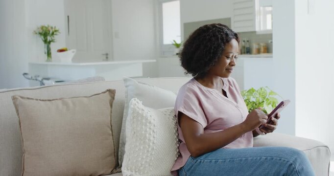 Checking messages, woman in pink blouse and jeans tapping pink-case phone on sofa, copy space