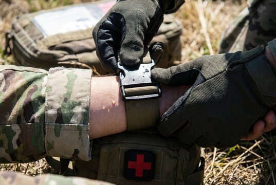Military medic hands applying a black tactical tourniquet to an arm to stop bleeding