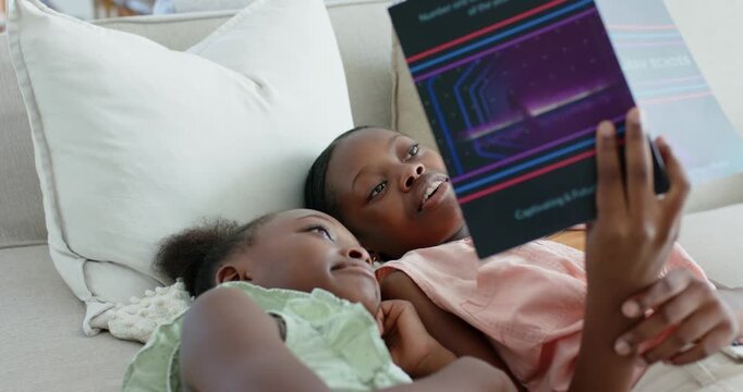 Vertical video: Holding purple book, big sister in pink top reading on couch to make sister laugh