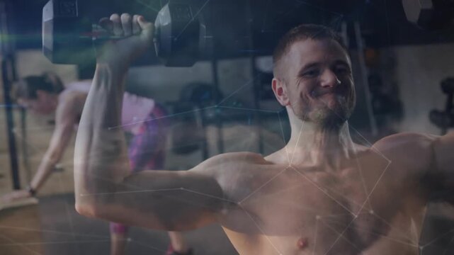 Taking breath shirtless man pressing hex dumbbells overhead at gym, woman in pink top stretching