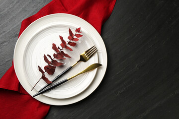 Naklejka premium Stylish setting with cutlery, napkin and branch on black table, top view