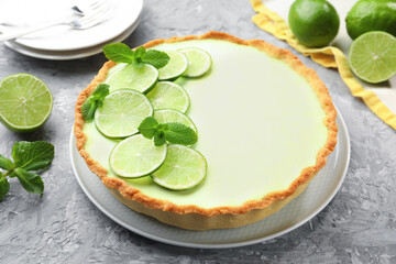 Tasty lime pie with fruit slices and mint leaves on grey textured table, closeup © New Africa