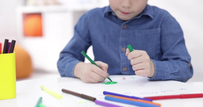 Little boy drawing with felt tip pens at white table indoors, closeup