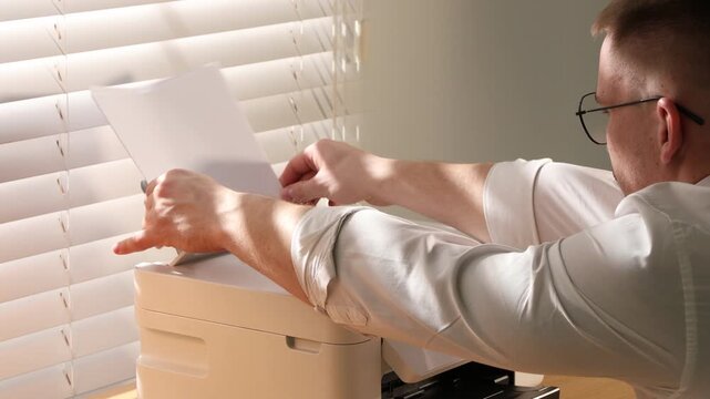 Man loading paper into printer at wooden desk indoors, closeup