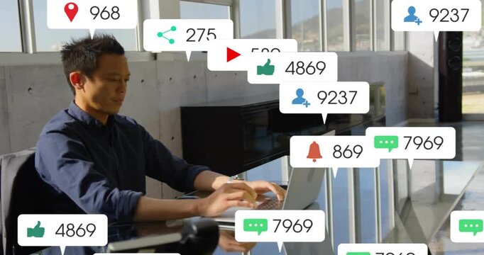 Mature Asian man navy-shirted typing at glass table in office with silver laptop and notifications