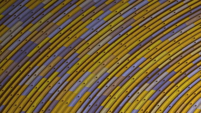Abstract pattern of curved yellow and purple metallic strips with small dark dots, creating a textured surface.