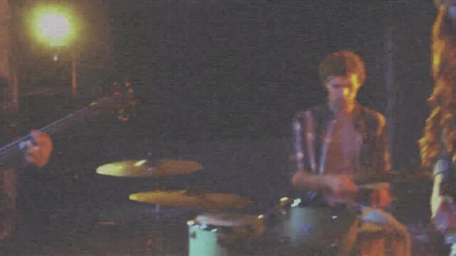 Snare sticks striking, camera pulling back, band playing music showing lead vocalist into mic