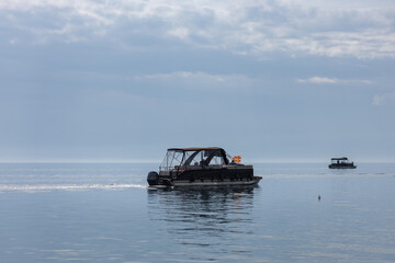 Obraz premium pontoon boat with macedonian flag cruising on calm blue lake water under a cloudy sky, tranquil summer travel and vacation concept