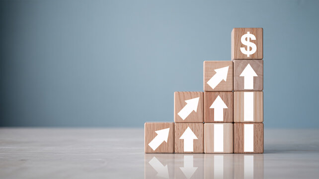 A stack of wooden blocks with arrows and a dollar sign, symbolizing financial growth and success.