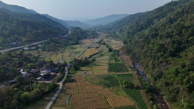 Aerial View of Lush Green Valley with Rice Fields, Surrounded by Mountains and Small Village, Under Clear Sky, Serene and Expansive Landscape