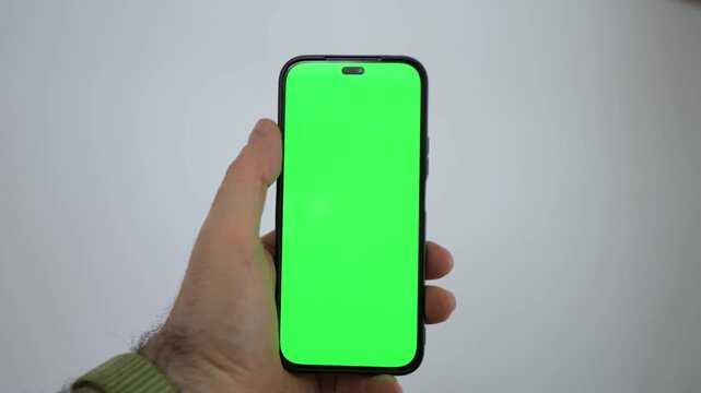 Hand holds smartphone with green screen. Phone has black frame and no visible brand. Background is plain white. Three keyframes show slight hand movement. No animals or plants visible