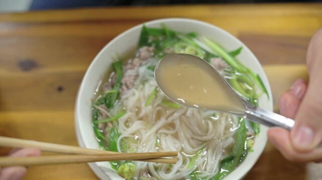 Taster Enjoys Flavorful Beef Broth. Caucasian Critic Tastes Vietnamese Pho With Greens And Tender Beef. An Intimate Shot Capturing Critic Savoring Vietnamese Pho With Greens And Aromatic Broth